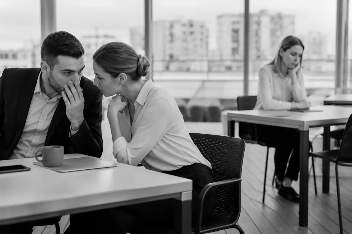 Salariée isolée pendant que des collègues chuchotent, illustration d'une situation de harcèlement au travail